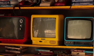 A collection of vintage retro TVs and old telephones on a wooden shelf, evoking nostalgia.