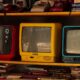 A collection of vintage retro TVs and old telephones on a wooden shelf, evoking nostalgia.