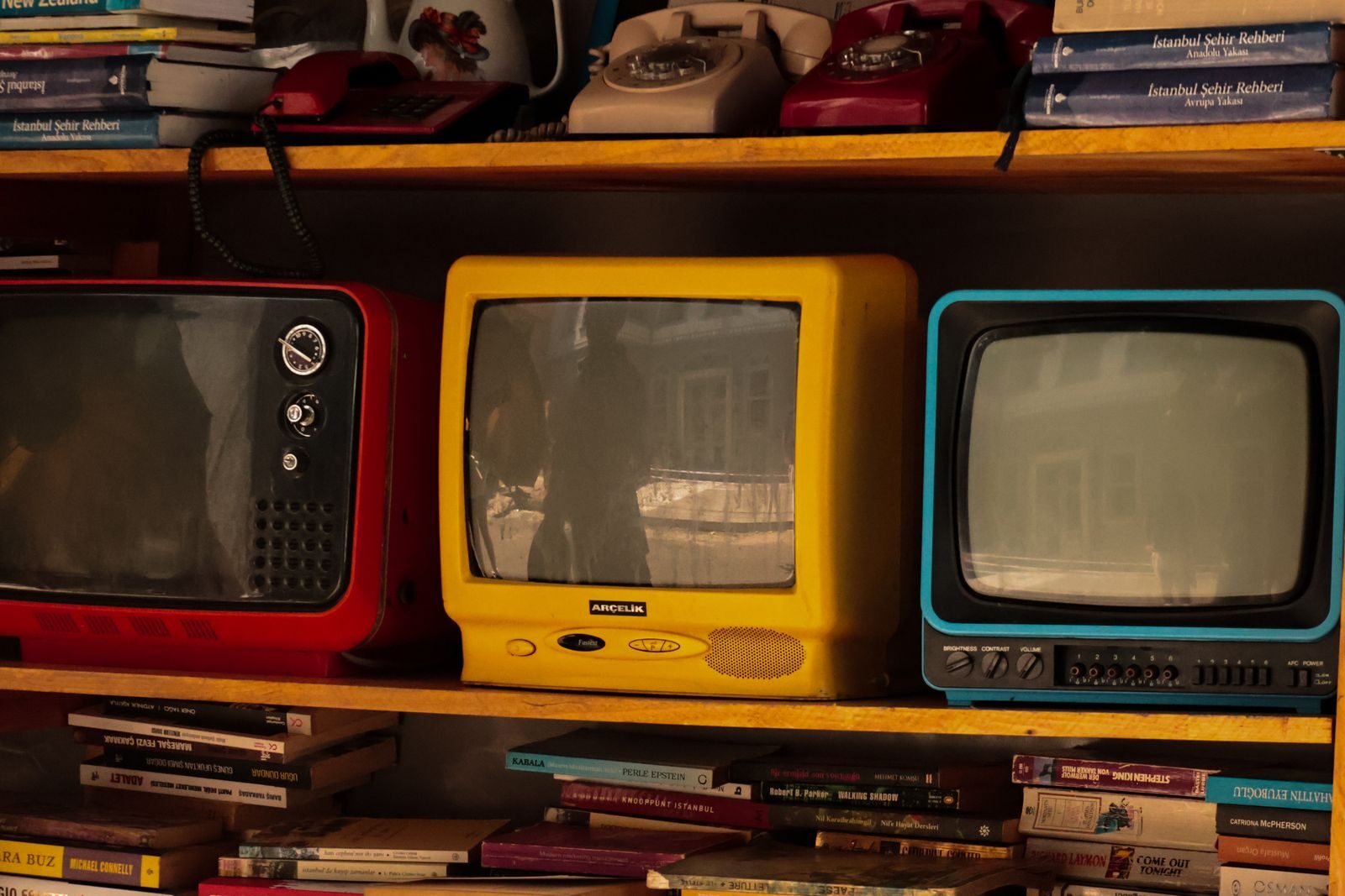A collection of vintage retro TVs and old telephones on a wooden shelf, evoking nostalgia.