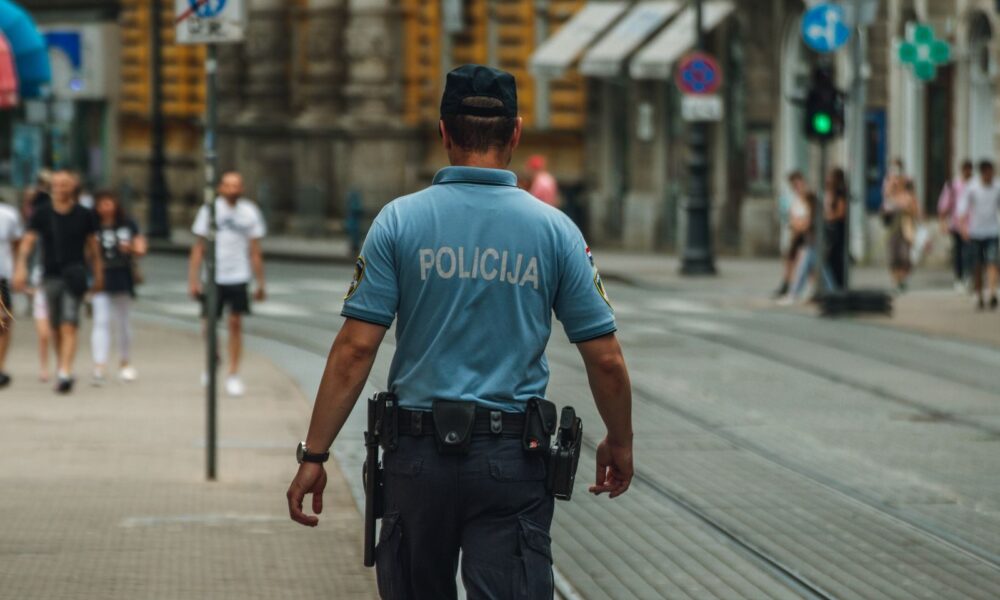 A police officer walking down a city street during the day, maintaining law and order.