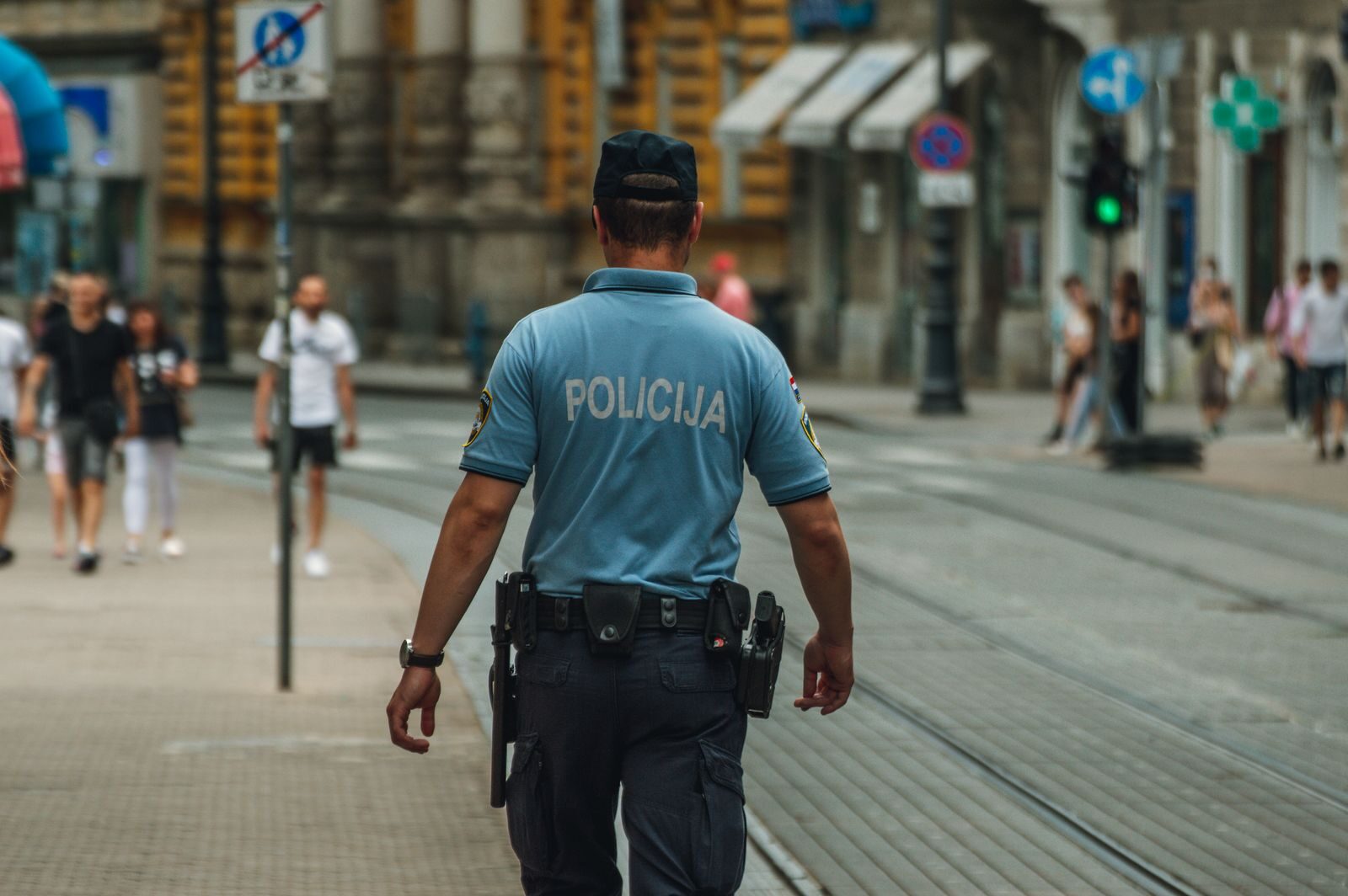 A police officer walking down a city street during the day, maintaining law and order.