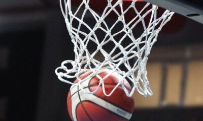 A basketball going through a hoop in an indoor sports arena captured mid-action.