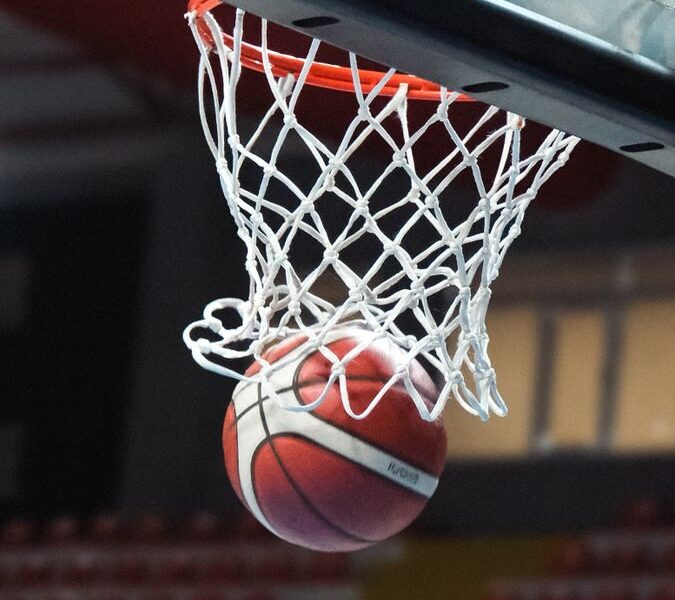 A basketball going through a hoop in an indoor sports arena captured mid-action.