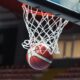 A basketball going through a hoop in an indoor sports arena captured mid-action.