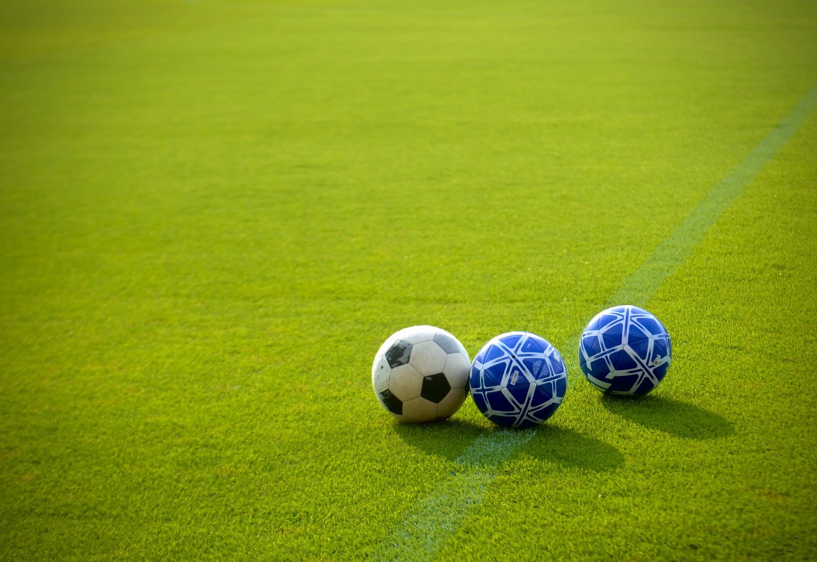 Three soccer balls positioned on a vibrant green field in the afternoon sun, perfect for sports themes.