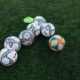 Group of soccer balls on a green grass field with a training cone, perfect for sports themes.