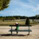 A woman in a green dress and hat relaxes on a bench in Fontainebleau Gardens, France, under a clear blue sky.
