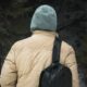 A man with a backpack hikes through a rainy forest wearing a hoodie and jacket.