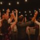 Group of adults dancing energetically under string lights at night.