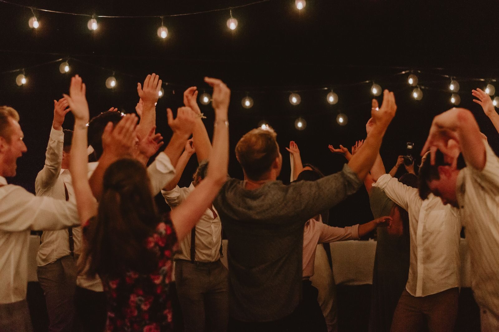 Group of adults dancing energetically under string lights at night.