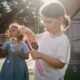 Two children joyfully creating bubbles, enjoying outdoor play under the sun.