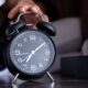 A hand reaches out to turn off an analogue alarm clock in the early morning.