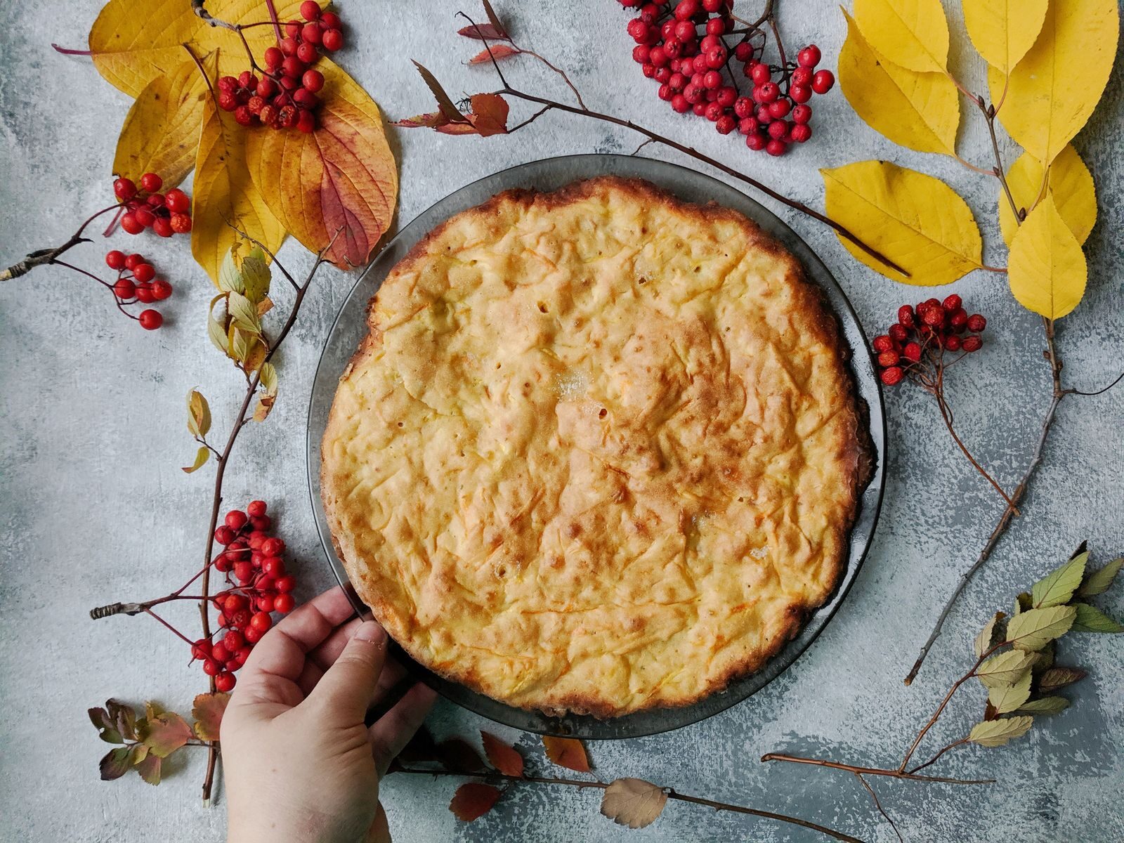 Freshly baked pie surrounded by autumn leaves and rowanberries on a rustic table.