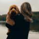 A woman holds her Labradoodle near a river under a cloudy sky in Düsseldorf.
