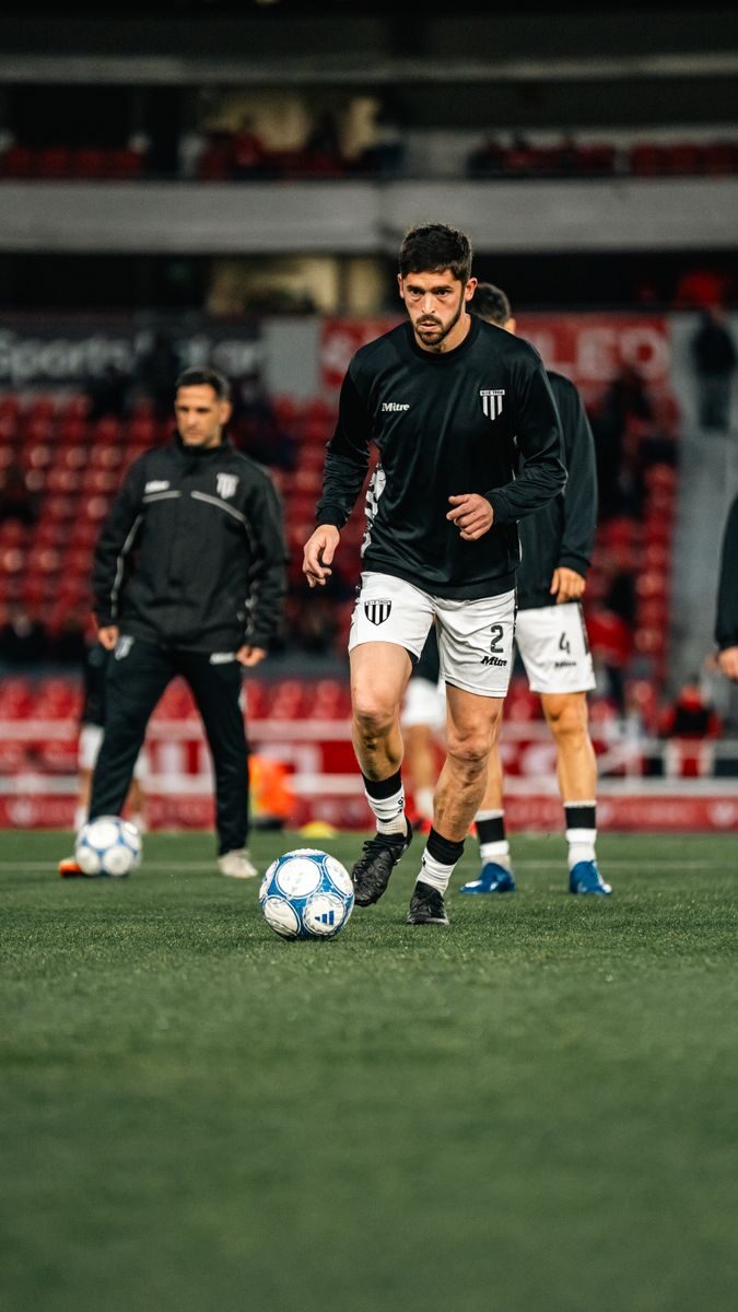 Soccer players in black jerseys warming up on a stadium field pre-match.