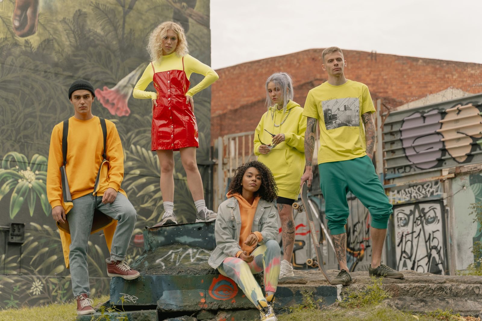 Fashionable group posing in vibrant street style against graffiti mural backdrop.