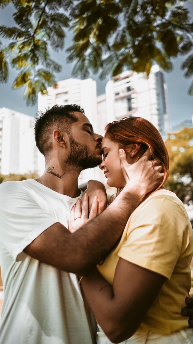 A loving couple shares a tender kiss under city trees, embodying youthful romance.