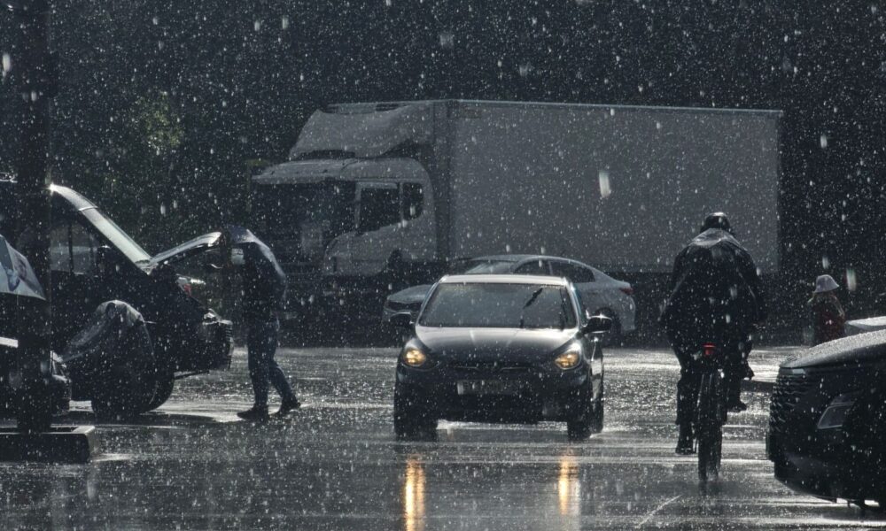Moody urban street scene in heavy rain with cars and pedestrians.
