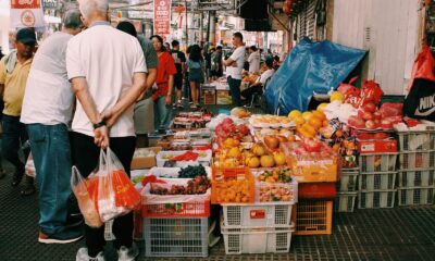 Lively street market with diverse fruits and people bustling in an urban setting.