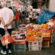 Lively street market with diverse fruits and people bustling in an urban setting.