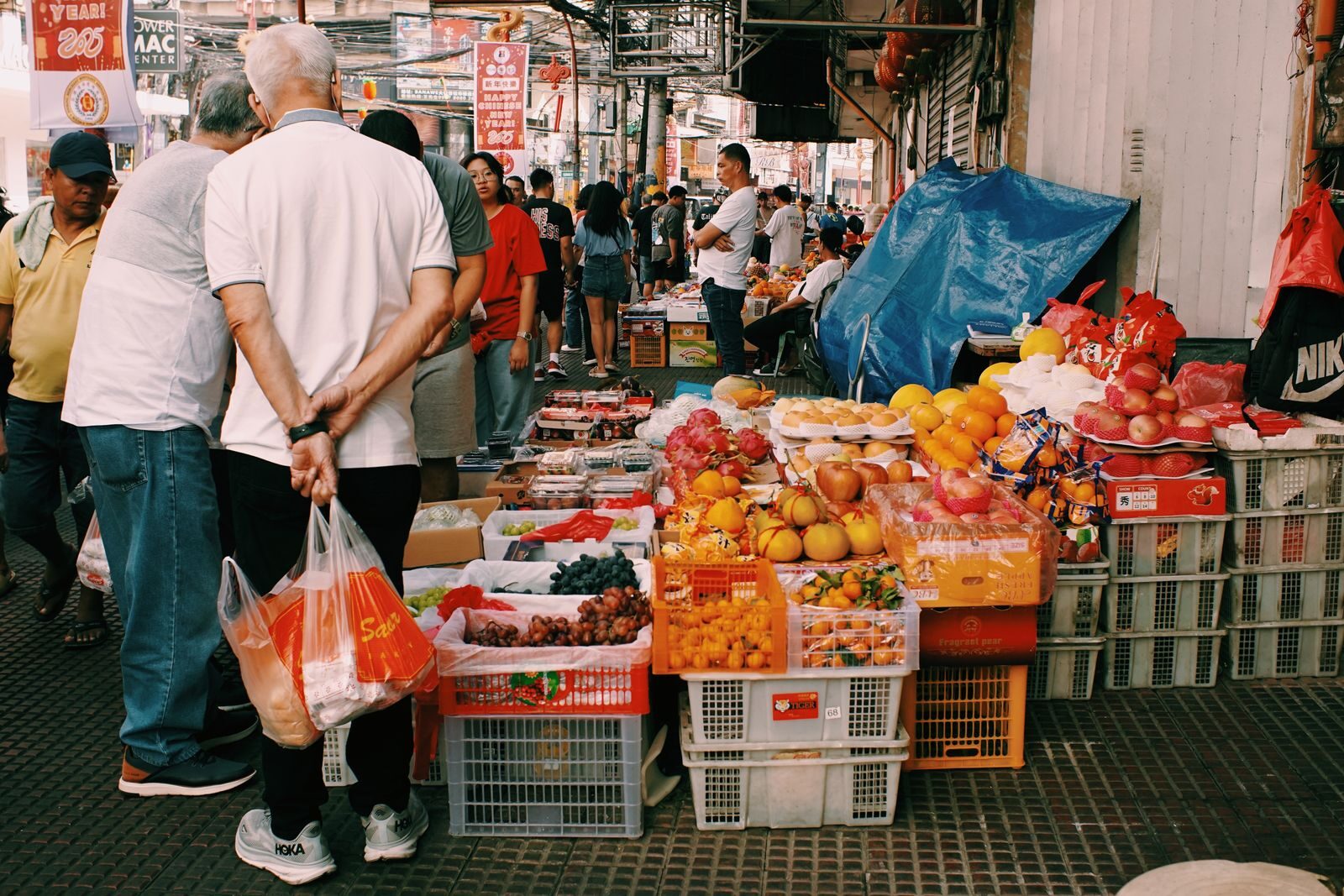 Lively street market with diverse fruits and people bustling in an urban setting.