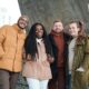 A group of four friends in winter attire smiling outdoors, enjoying togetherness.