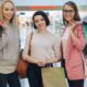 Three smiling women with shopping bags inside a mall, enjoying a day out.