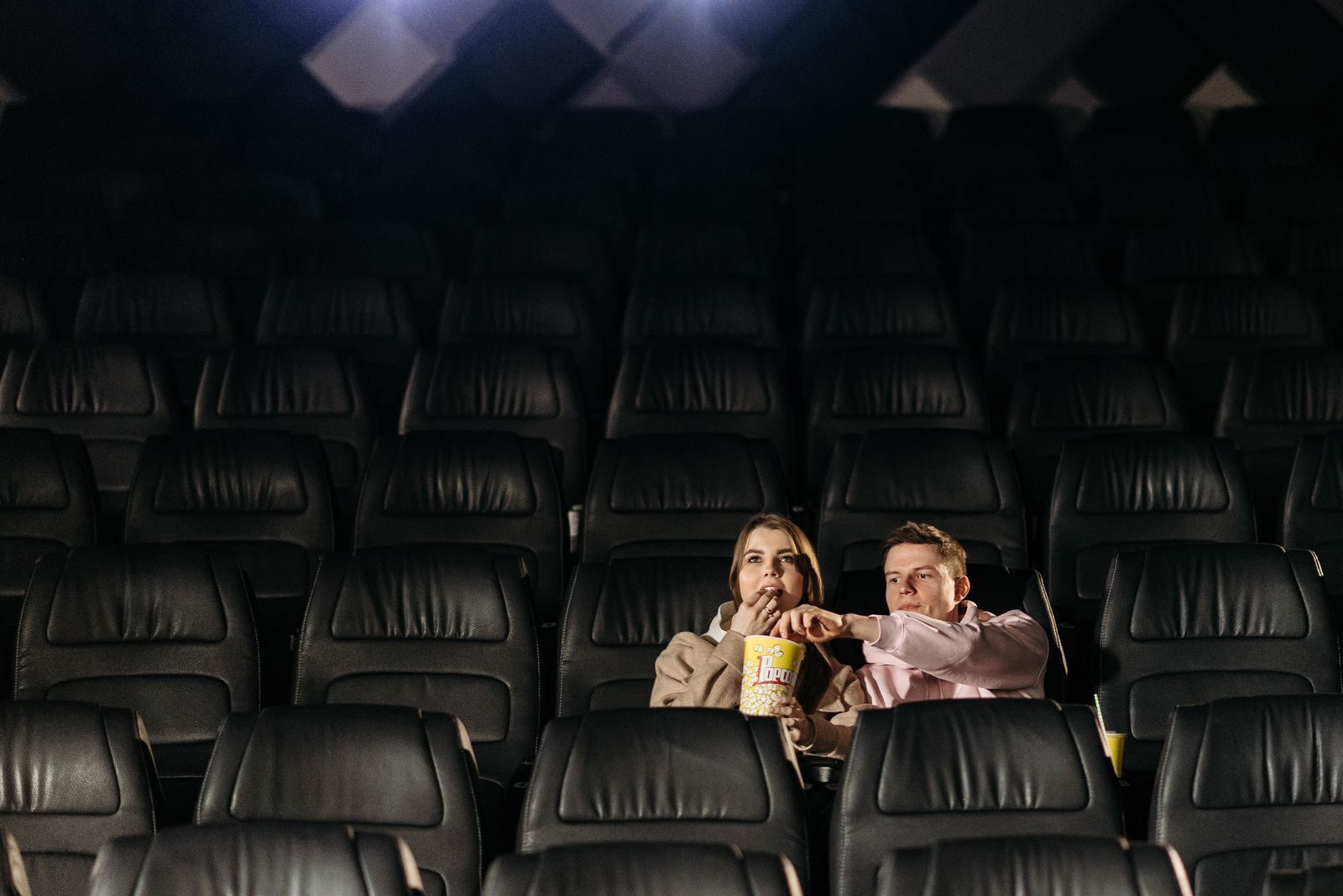 A couple enjoying a movie date with popcorn in an empty theater.