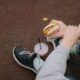 Person sitting outdoors enjoying a cheeseburger with a drink, captured from above.