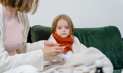 A caring moment of a woman checking a sick child's temperature on a cozy green couch indoors.