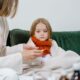 A caring moment of a woman checking a sick child's temperature on a cozy green couch indoors.