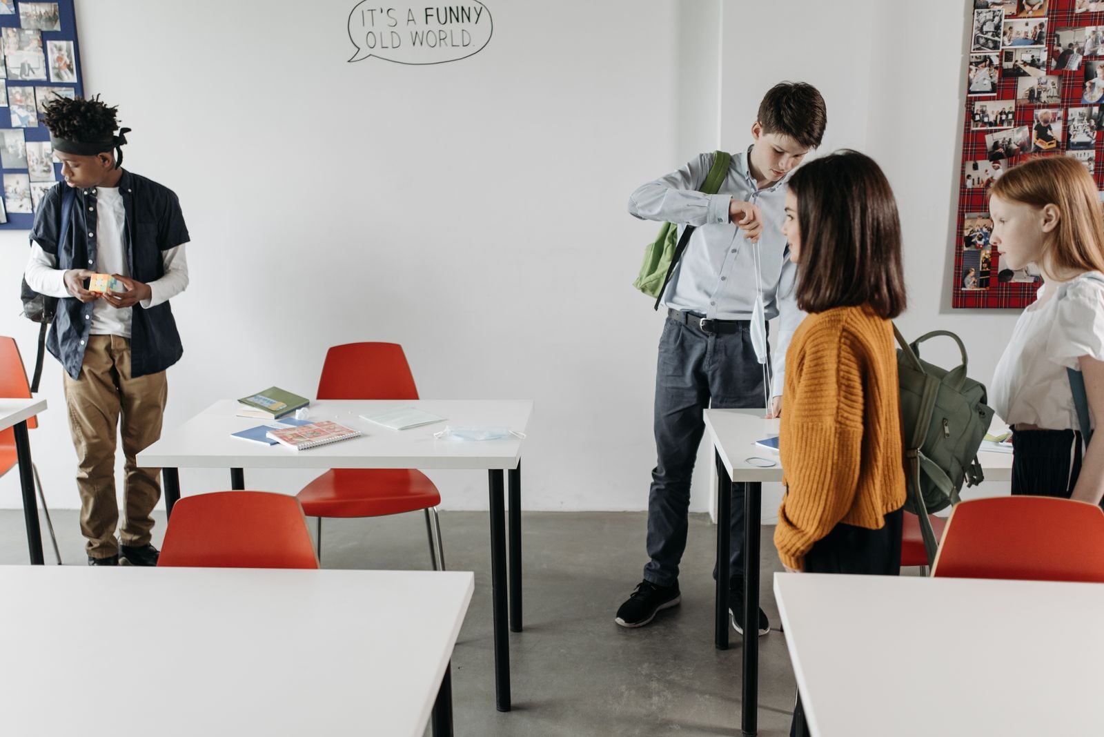 Students socializing in a classroom with red chairs and white desks, preparing to leave.