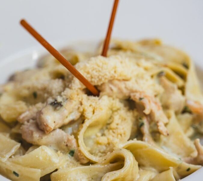 Close-up of creamy pasta with chicken and parmesan in a white bowl, perfect for dining themes.