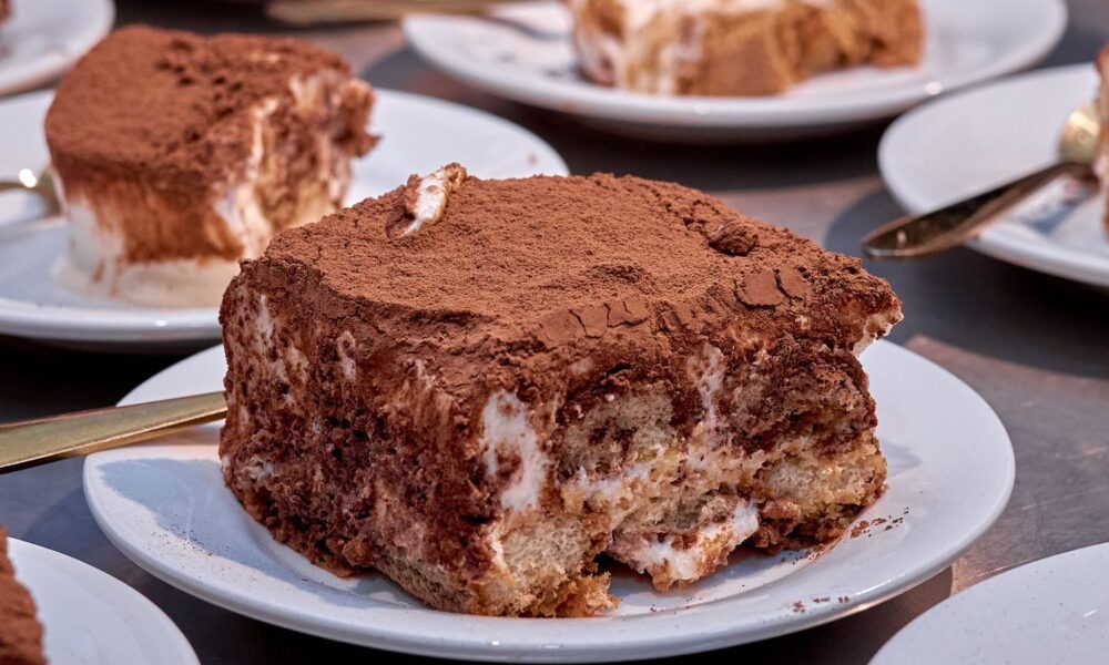 Close-up of a delectable tiramisu dessert on a white plate, dusted with cocoa powder.