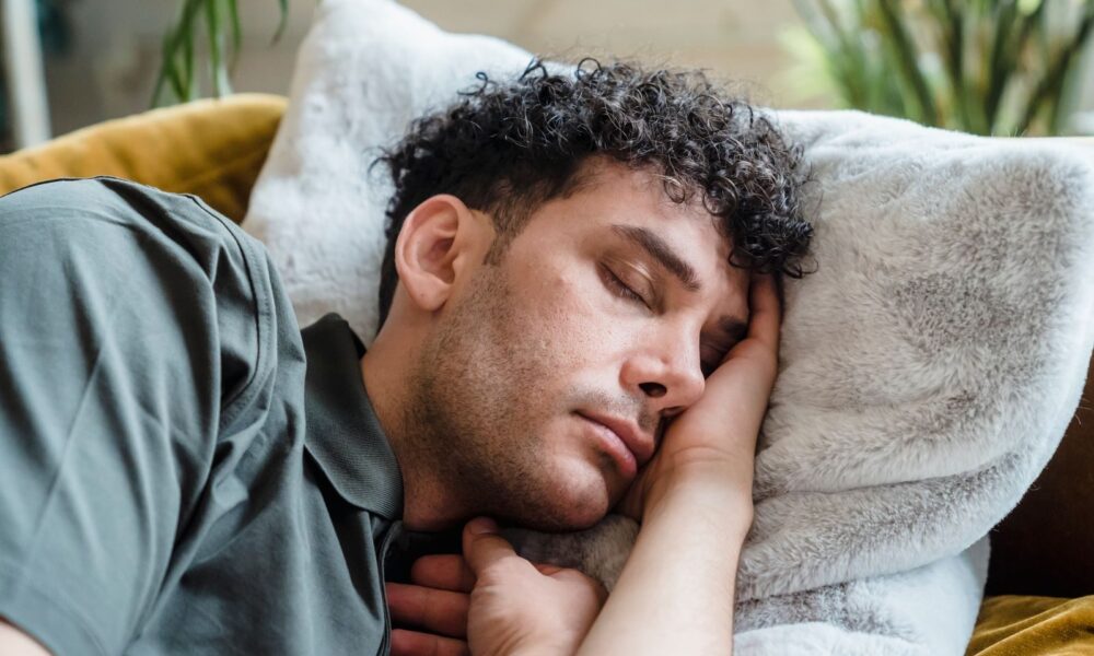 A young man with curly hair peacefully sleeping on a cozy couch with a soft pillow.