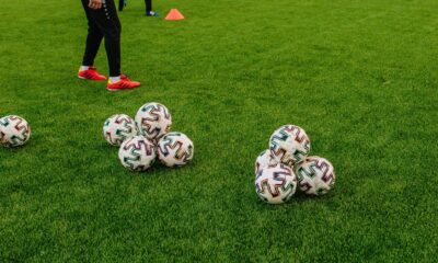 Pile of soccer balls on a green field with a person preparing for training session.