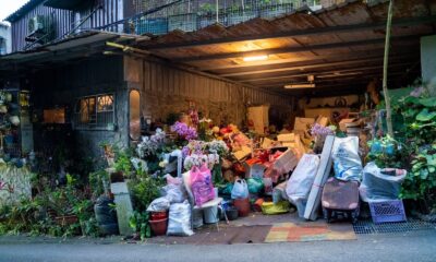 A garage filled with various household items, plants, and clutter overflowing onto the street.