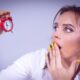 A surprised woman with yellow nails holds a small red alarm clock against a white backdrop.