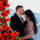 A couple shares a tender moment surrounded by vibrant red roses, creating a romantic atmosphere.