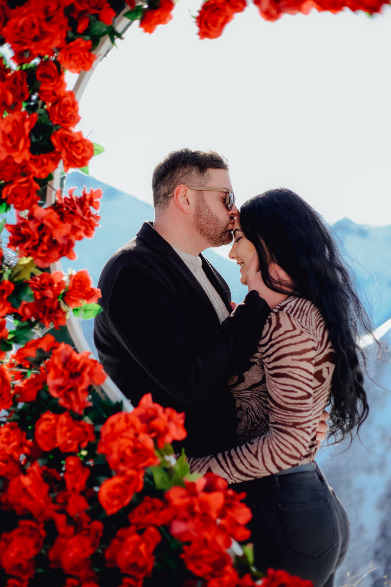 A couple shares a tender moment surrounded by vibrant red roses, creating a romantic atmosphere.