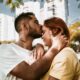 A loving couple shares a tender kiss under city trees, embodying youthful romance.