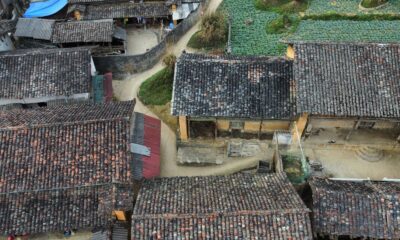 Aerial shot of a rustic village with traditional tiled roofs surrounded by farmland and pathways.