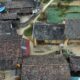 Aerial shot of a rustic village with traditional tiled roofs surrounded by farmland and pathways.