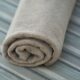 Close-up of a soft beige cotton towel rolled neatly on a striped fabric surface. Perfect for home decor or textile themes.