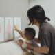 A mother and child engage in a learning activity, exploring art drawings in a cozy indoor setting.