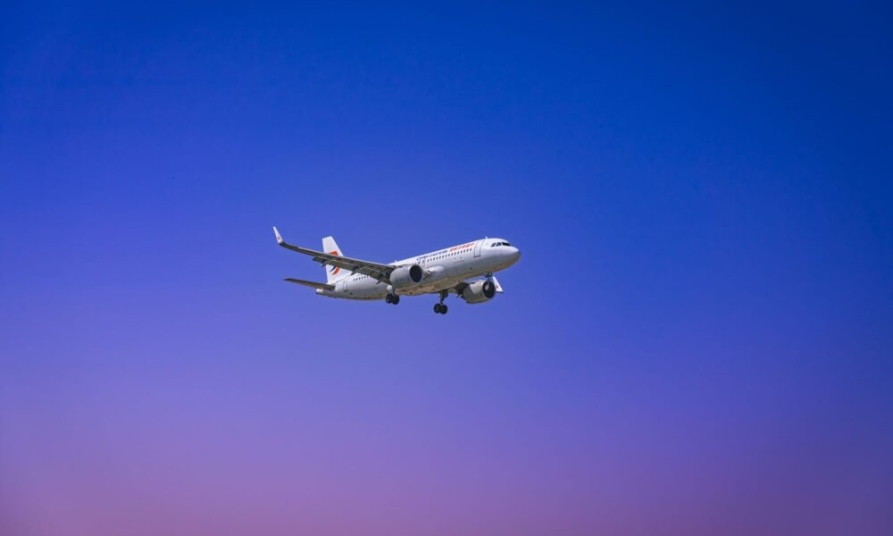 A commercial airplane flying through a clear blue and purple sky during daytime.