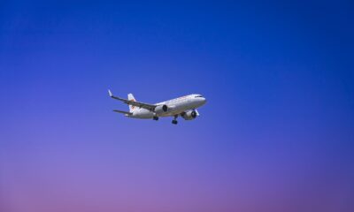A commercial airplane flying through a clear blue and purple sky during daytime.