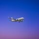 A commercial airplane flying through a clear blue and purple sky during daytime.