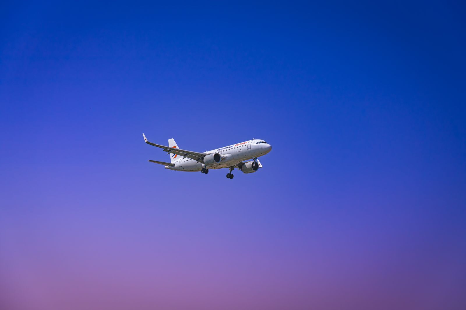 A commercial airplane flying through a clear blue and purple sky during daytime.