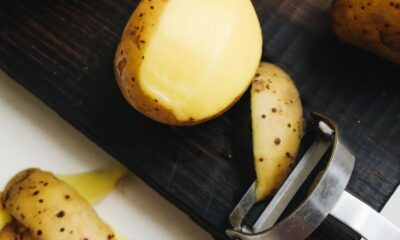 Close-up of potatoes and peeler on a cutting board, ready for cooking.